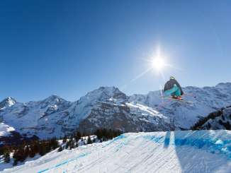 Ein Skifahrer auf der Skicrosspiste im Skigebiet Mürren-Schilthorn. Das Dreigestirn Eiger, Mönch und Jungfrau ist aus der Ferne zu sehen.