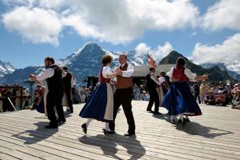 At the Mountain Spring Festival on the Männlichen, people dance against the backdrop of the Eiger. The dancers are dressed in traditional costumes.