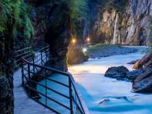Abendstimmung in der Aareschlucht. Der Steg entlang des Wassers ist beleuchtet. Durch das Licht färben sich die Felswände in einem wohligen Gelb.