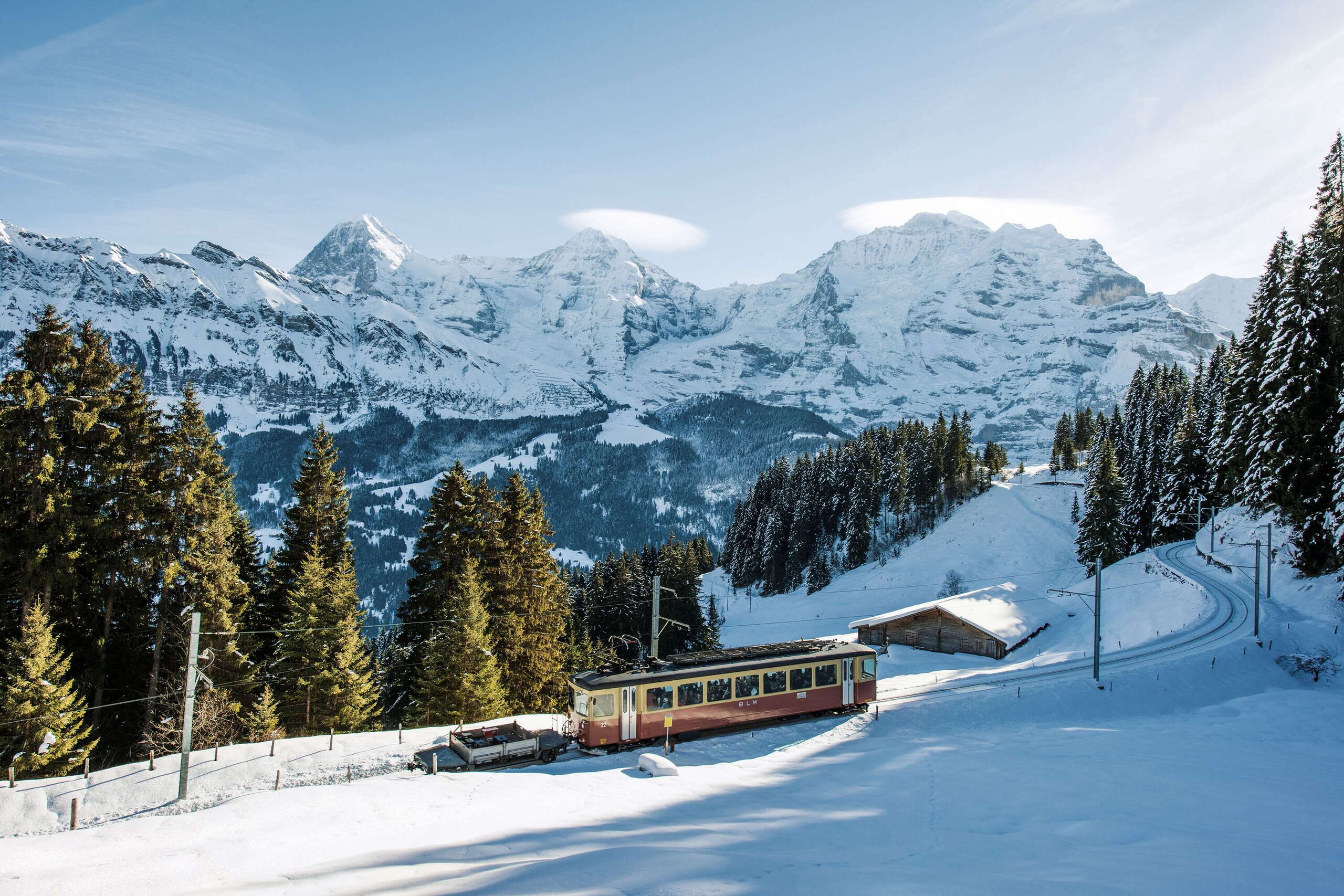 Die BLM fährt von der Grütschalp nach Mürren. Im Hintergrund ist das verschneite Bergpanorama von Eiger, Mönch und Jungfrau zu sehen.