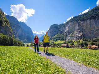 Wanderer laufen durch das Lauterbrunnental. Die steilen Felswände ragen gegen den Himmel.