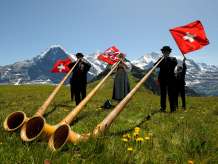 Am Bergfrühlingsfest auf dem Männlichen spielen drei Musiker*innen das Alphorn auf der Wiese.