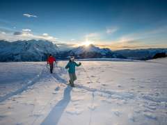 Im Sonnenuntergang - und vor eindrücklicher Bergkulisse: Zwei Schneeschuhläufer*innen unterwegs am Hasliberg