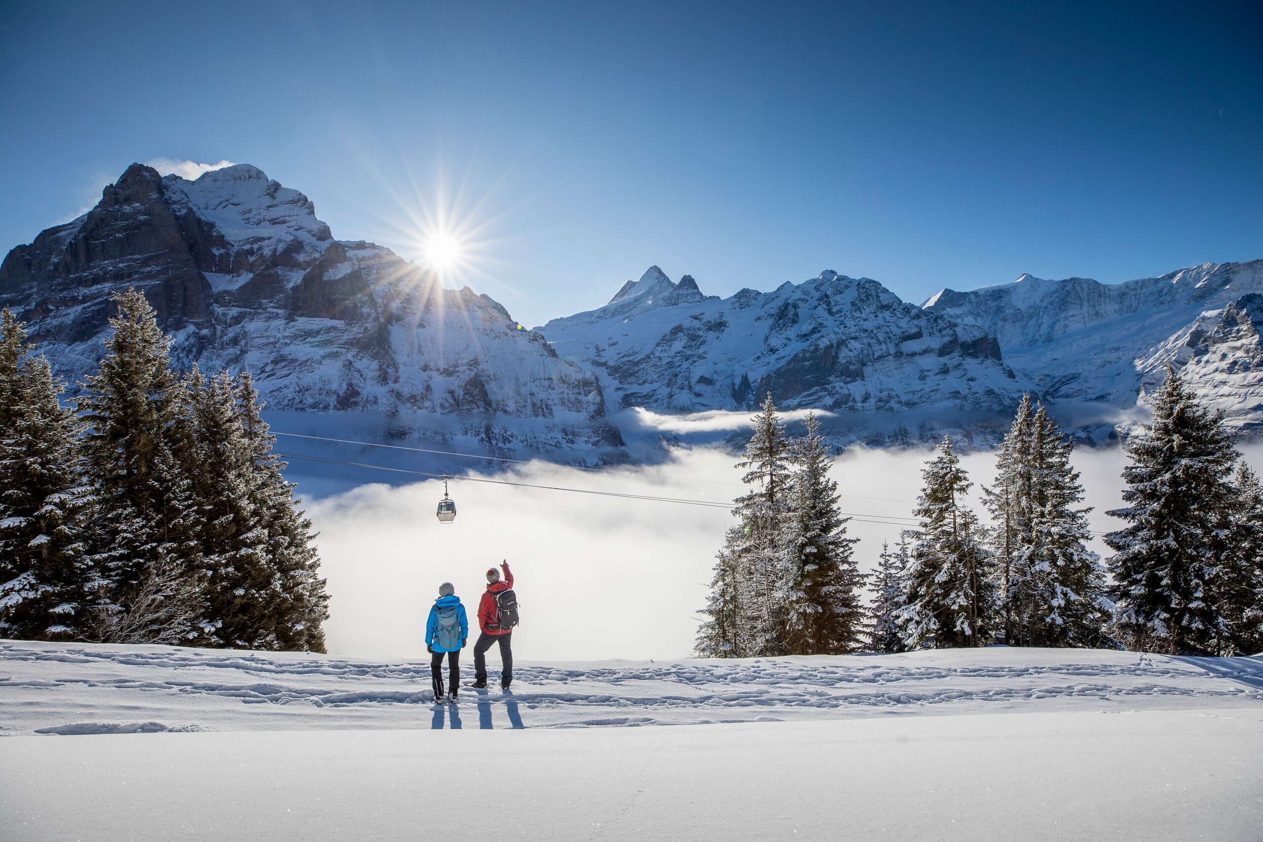 Winter hike on snow-covered winter hiking trails around Grindelwald. The hikers enjoy the sunny day and impressive views of the Eiger.