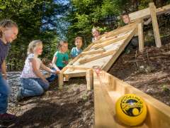 Die Kinder spielen an den fix installierten Holzmurmelbahnen am Kugelweg im Hasliberg.