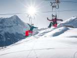 Drei Personen rasen mit dem First Flyer den Berg hinunter. Im Hintergrund scheint die Sonne über dem verschneiten Eiger.