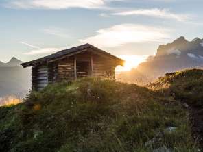 Cabane en bois située sur une colline près du Männlichen, avec le soleil bas et un panorama alpin en toile de fond.
