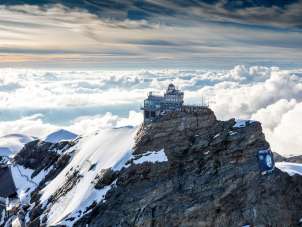 Blick von oben auf das Jungfraujoch, umgeben von Schnee, im Hintergrund ein Nebelmeer.