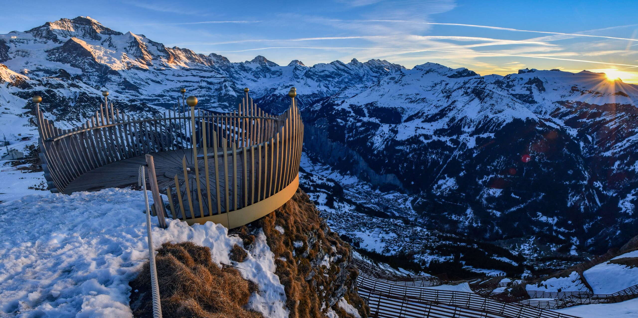 The crown of the Royal Walk is illuminated by the setting sun. The snow-covered mountain panorama in the background lends the region around Wengen a magical atmosphere.