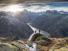 Zwei Wanderer unterwegs in der Grimselwelt. Sie wandern vor einmaliger Aussicht auf einen Stausee der Grimselwelt.