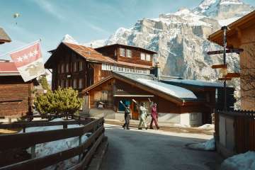 Drei Wintersportler*innen gehen mit ihren Skiern durch Mürren.