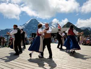 Am Bergfrühlingsfest auf dem Männlichen wird vor dem Panorama mit dem Eiger getanzt. Die Tänzer*innen sind in traditionellen Trachten gekleidet.