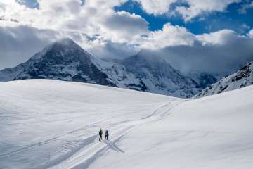 Winterwanderung auf verschneiten Winterwanderwegen rund um Grindelwald. Die Wanderer geniessen den sonnigen Tag und imposanten Ausblick auf den Eiger.