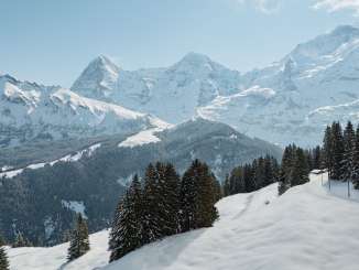 Vue d'en haut, on admire le paysage enneigé qui borde la ligne BLM entre Grütschalp et Mürren. La ligne ferroviaire traverse des pentes blanches, longeant ici et là des chalets isolés et des sapins, avec une vue imprenable sur les montagnes environnantes.