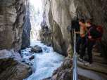 Au fil des siècles, la rivière a sculpté les gorges du glacier de Rosenlaui. Le sentier longe la paroi rocheuse surplombant la rivière et s'enfonce dans les gorges. Depuis la passerelle, les deux randonneurs admirent la rivière dans les gorges de Rosenlaui.