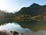 Das Sulsseeli oberhalb der Lobhornhütte liegt eingebettet in einer alpinen Berglandschaft. Die ruhige Wasseroberfläche spiegelt die umliegenden Gipfel und Hänge, während die tief stehende Sonne für eine stimmungsvolle Atmosphäre sorgt.