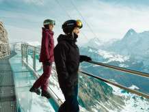 Zwei Frauen in Skiausrüstung geniessen das Winter-Bergpanorama mit dem Eiger auf dem Thrill Walk.