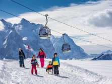Winter im Haslital: Eine junge Familie beim Schlitteln am Hasliberg. Im Hintergrund Gondeln der Bergbahnen Meiringen-Hasliberg - und die eindrückliche Bergwelt des Haslitals.