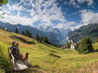 Hiking in Wengen across green meadows. The hikers enjoy the view of the Lauterbrunnen Valley from a bench.
