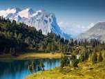 Le lac d'Engstlen est entouré de prairies verdoyantes et de conifères. En arrière-plan, on aperçoit les sommets enneigés.