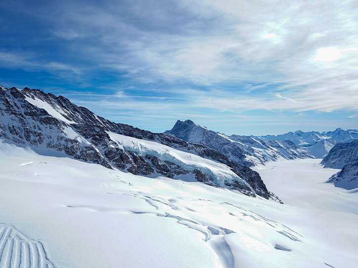 Le glacier d'Aletsch en hiver, avec une large couche de neige, entouré de sommets enneigés sous un ciel dégagé.