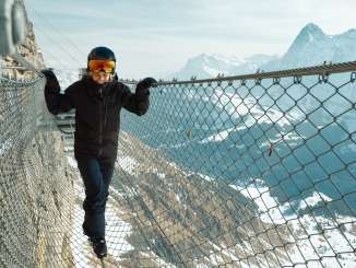 Eine Frau balanciert auf einem Drahtseil beim Felsensteg Thrill Walk mit eindrücklichem Winter-Bergpanorama mit dem Eiger im Hintergrund.
