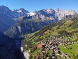 Aerial view of the village of Mürren. The village is surrounded by green meadows and forests. The Lauterbrunnen Valley is characterized by its steep rock faces.