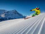 Skiing at the Grindelwald First ski resort. Skiers carve beautiful turns through the snow. In the background, you can see the Eiger.