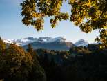 Herbstlich gefärbte Blätter rahmen den Blick auf eine Berglandschaft mit verschneiten Gipfeln.