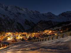 Das verschneite Dorf Mürren leuchtet bei Nacht in einer goldigen Farbe. Im Hintergrund ist das Bergpanorama in der Dunkelheit knapp zu erkennen.