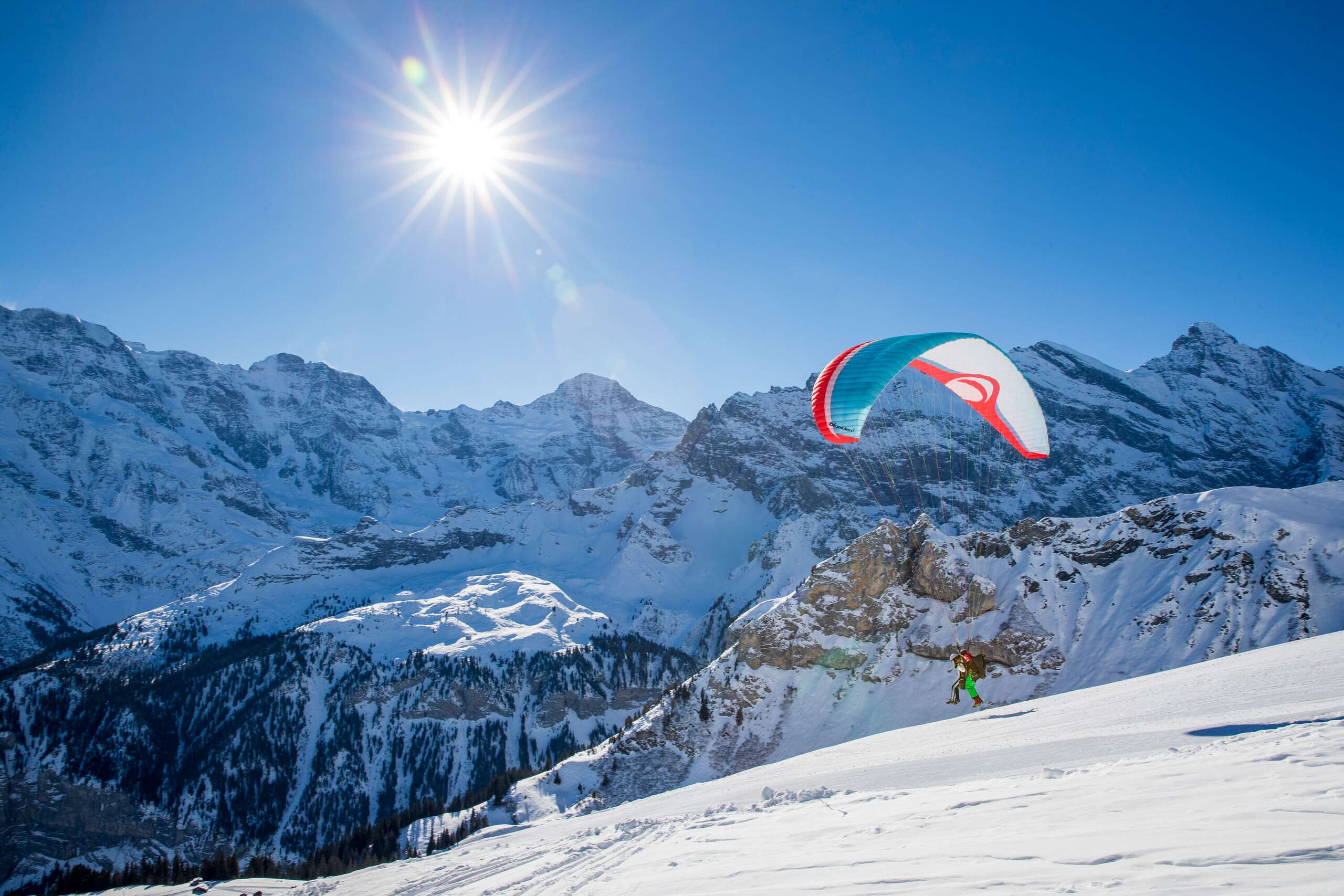 Décollage pour un vol hivernal en parapente. Le décollage se fait sur une piste préparée. Le panorama de montagne avec le Gspaltenhorn se montre magnifiquement au soleil.