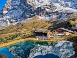 Das Bergrestaurant Kleine Scheidegg steht oberhalb eines kleinen Bergsees. Im Hintergrund erheben sich der Eiger und der Mönch, deren markante Fels- und Schneeflanken sich im ruhigen Wasser spiegeln.