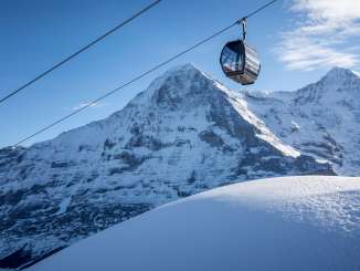 The Eiger, covered in snow, can be seen in the background behind a gondola from the Grindelwald–Männlichen cable car.