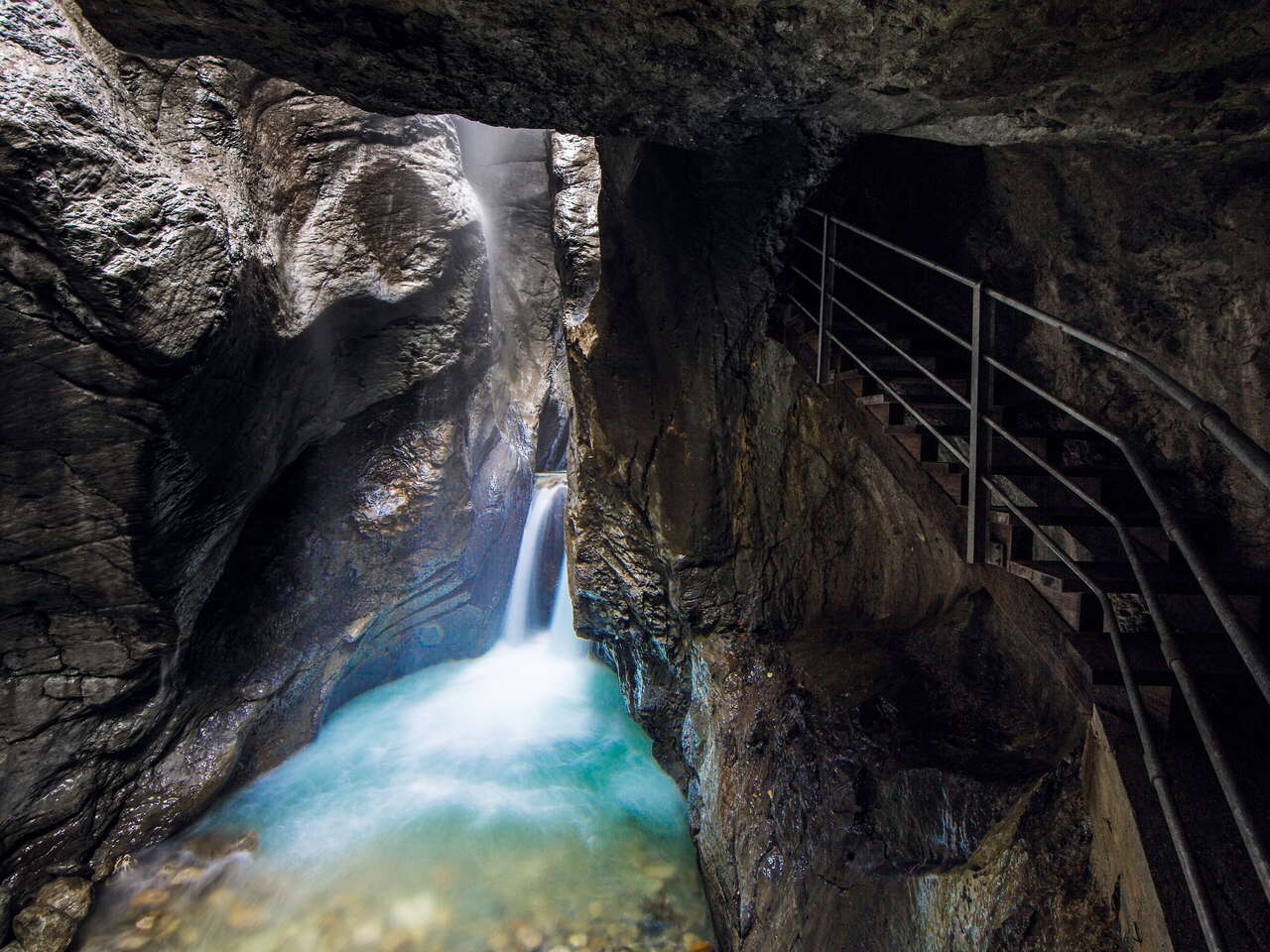 Die Rosenlauischlucht lässt nur wenig Licht zu welches den Fluss und den kleinen Wasserfall schön beleuchtet. Der Steg ist in den Felsen gehauen.