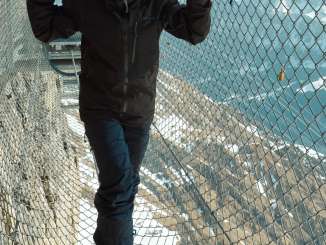 Une femme marche en équilibre sur un fil métallique au « Thrill Walk », une passerelle suspendue au-dessus des rochers, avec un panorama hivernal impressionnant sur les montagnes, l'Eiger en arrière-plan.