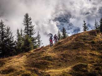 Deux cyclistes sont à vélo et empruntent la piste North Face. Le panorama montagneux en arrière-plan est enveloppé de nuages.