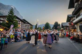 Ein Kreis aus Tänzerinnen und Tänzern in Tracht bewegt sich im Rhythmus der Musik durch das Dorfzentrum von Grindelwald – gelebte Schweizer Tradition.