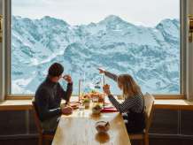 Zwei Personen geniessen einen Brunch im 360°-Restaurant Piz Gloria auf dem Schilthorn. Während des Essens eröffnet sich durch die grossen Panoramafenster ein eindrucksvoller Blick auf die verschneite Bergwelt.