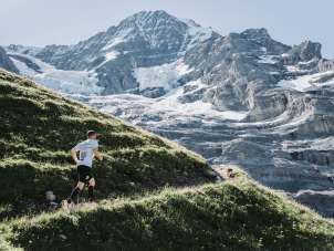 A runner on the mountain course of the Jungfrau Marathon. Scattered snowfields and glaciers on the mountain can be seen in the background.