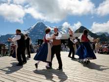 Am Bergfrühlingsfest auf dem Männlichen wird vor dem Panorama mit dem Eiger getanzt. Die Tänzer*innen sind in traditionellen Trachten gekleidet.