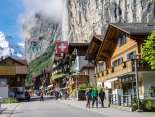 The village of Lauterbrunnen is surrounded by imposing cliffs. Tourists stroll through the village. The Staubbach Falls can be seen in the background.