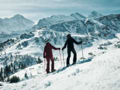 Zwei Wintersportlerinnen auf einer verschneiten Piste mit weiter Aussicht auf die schneebedeckte Berglandschaft in Mürren.