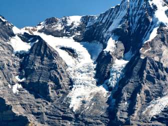 The Eiger and Mönch rise above the Alpine landscape with their steep rock faces and snow-covered slopes. Glacier fields and rocky passes are visible between the peaks.